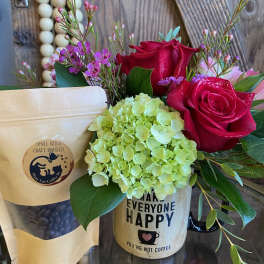 Mug arrangement with red roses and green hydrangea beside a kraft bag of coffee beans