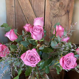Clear glass vase with pink roses and filler flowers on a woven mat