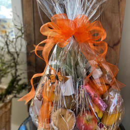 Cellophane-wrapped fruit and snack gift basket with a large orange bow and butterfly accent.
