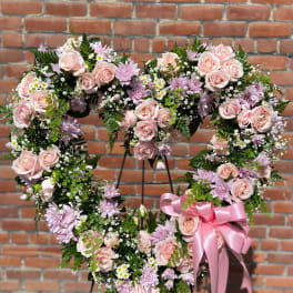 Heart-shaped standing wreath of pink roses and lavender mums with a pink bow on an easel