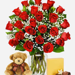 Red roses in a glass vase with a teddy bear and chocolates