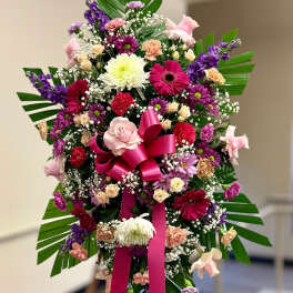 Tall standing spray of pink, purple, and white flowers with a large hot pink bow on an easel