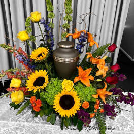 Cremation urn surrounded by bright sunflowers, lilies, roses, and mixed blooms on a table