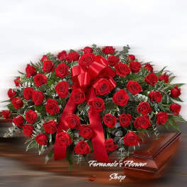 Red rose casket spray with a large red bow on a wooden casket