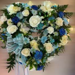 Heart-shaped wreath of white roses and blue carnations with a light blue ribbon bow