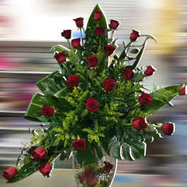 Tall arrangement of red roses with large tropical leaves in a clear glass vase