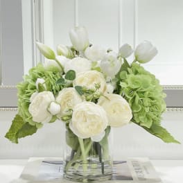 White tulips and cream roses in a clear glass vase with green hydrangeas