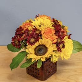 Sunflowers, roses, and mums arranged in a square brown vase