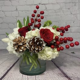 Red roses and white hydrangeas in a glass vase with pinecones and red berries