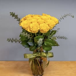 Yellow roses arranged in a glass vase with a green ribbon