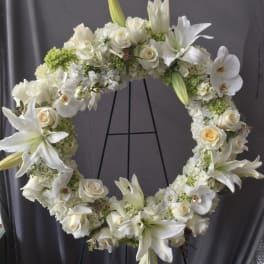 White floral wreath with roses and lilies on a black stand