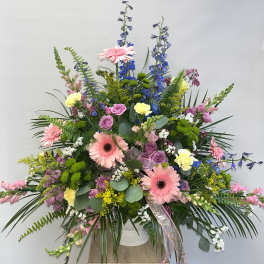 Large mixed floral arrangement with pink gerberas and blue delphinium in a white vase