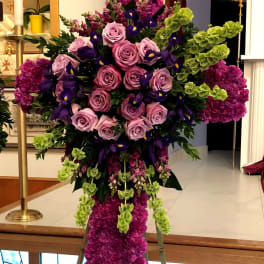 Tall cross-shaped standing spray of purple roses, irises and green bells of Ireland on an easel