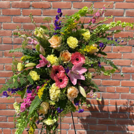 Tall standing spray with pink lilies, peach roses, and yellow flowers on an easel.