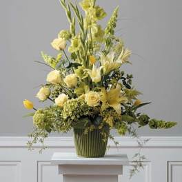 Tall yellow and green floral arrangement with roses, lilies, and tulips in a green ribbed pot