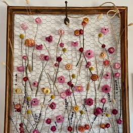 Rustic wall panel of dried pink and yellow flowers woven through chicken wire in a wooden frame