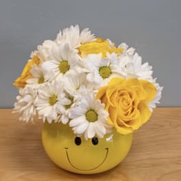 Yellow smiley-face vase holding white daisies and yellow roses