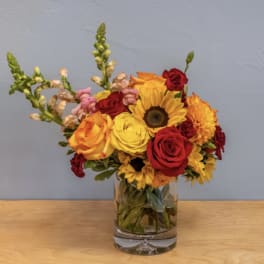 Mixed bouquet of roses, sunflowers, and snapdragons in a glass vase