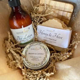 Gift box with bee-themed lotion, soap, candle, and wooden soap dish on kraft paper.