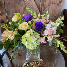 Mixed bouquet of yellow, purple, and pink flowers in a clear glass cube vase