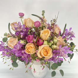 Mixed bouquet of peach roses and purple orchids in a white vase