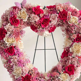 Heart-shaped floral wreath with pink and cream roses on a stand
