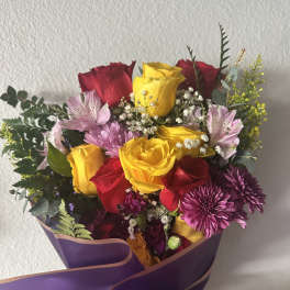 Bouquet of red and yellow roses with purple flowers wrapped in purple paper