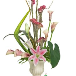 Tall arrangement of pink lilies and calla lilies with linear greenery in a cream urn vase.