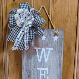 Wooden welcome sign with a black-and-white bow and bee ribbon