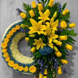 Standing wreath of yellow lilies and roses with blue and white flowers on a wooden easel
