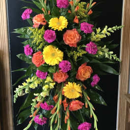 Tall standing spray of bright yellow, orange, and hot pink flowers on a metal easel.