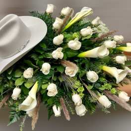 Sympathy spray of white roses and calla lilies with a light cowboy hat on top