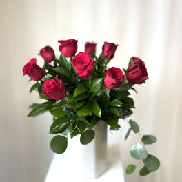 Bouquet of red roses with glossy greenery in a white vase