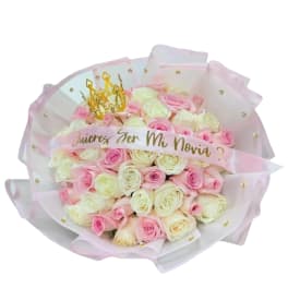 Round bouquet of pink and white roses wrapped in pink-edged paper with a gold crown decoration
