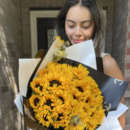 Woman holding a large bouquet of yellow sunflowers wrapped in black and white paper