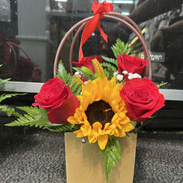 Red roses and a sunflower in a gold gift bag with a red ribbon