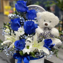 Blue roses and white lilies arranged with a teddy bear in a round box