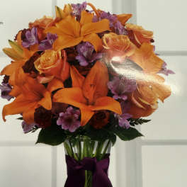 Orange lilies and roses in a clear vase with a purple ribbon
