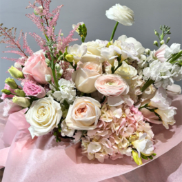 Hand-tied bouquet of white and blush roses, ranunculus and hydrangeas wrapped in pink tissue paper