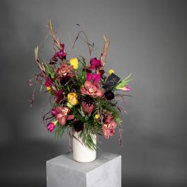 Tall bouquet of pink orchids and yellow tulips in a white vase