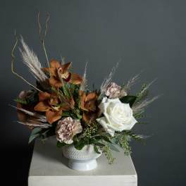 Arrangement of orange orchids, white rose, and pale pink carnations in a white vase