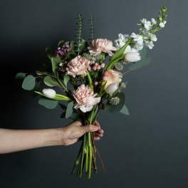 Handheld bouquet of pale pink and white flowers with greenery