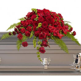 Red rose casket spray with trailing greenery on a gray casket