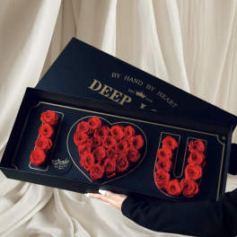 Red roses arranged in a heart and the word LOVE in a black gift box