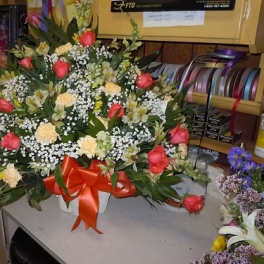 Large bouquet of pink roses and white filler flowers in a white basket with a red ribbon