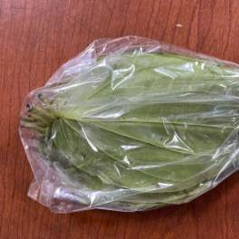 Plastic-wrapped bundle of green leaves on a wooden surface