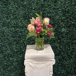 Small mixed flower arrangement in a clear glass vase on a white pedestal