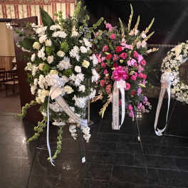 Three funeral wreaths with white and pink flowers on stands