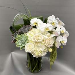 White orchids, roses, hydrangea, and succulents in a clear glass vase