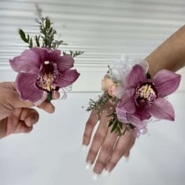 Two purple orchid wrist corsages held in hands.